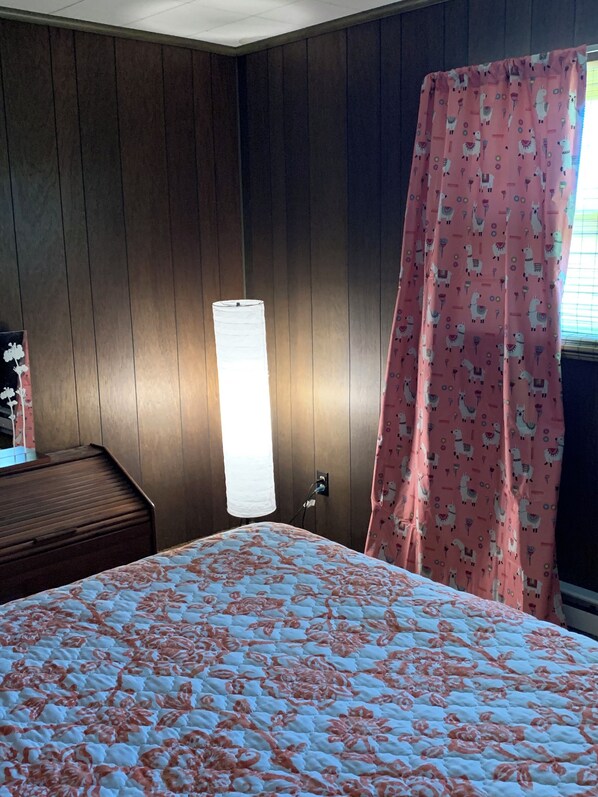 A room with a bed, a nightstand, a lamp, and a curtain with a pattern. - Family retreat! Comfortable Country Farmhouse 5 minutes south of Sparta. (Sparta)