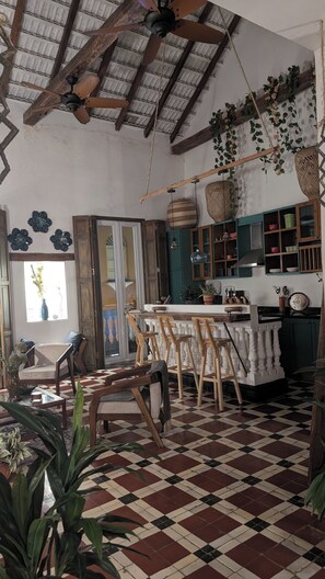Een ruime keuken met een zwart-wit schakeerd vloer, houten stoelen, een eettafel en hangende planten.