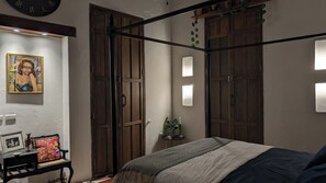 A bedroom with a four-poster bed, a bedside table with a lamp, a wall clock, and a framed picture. - Old City 2-bedroom, 2-bath Condo with Patio (Cartagena de Indias)