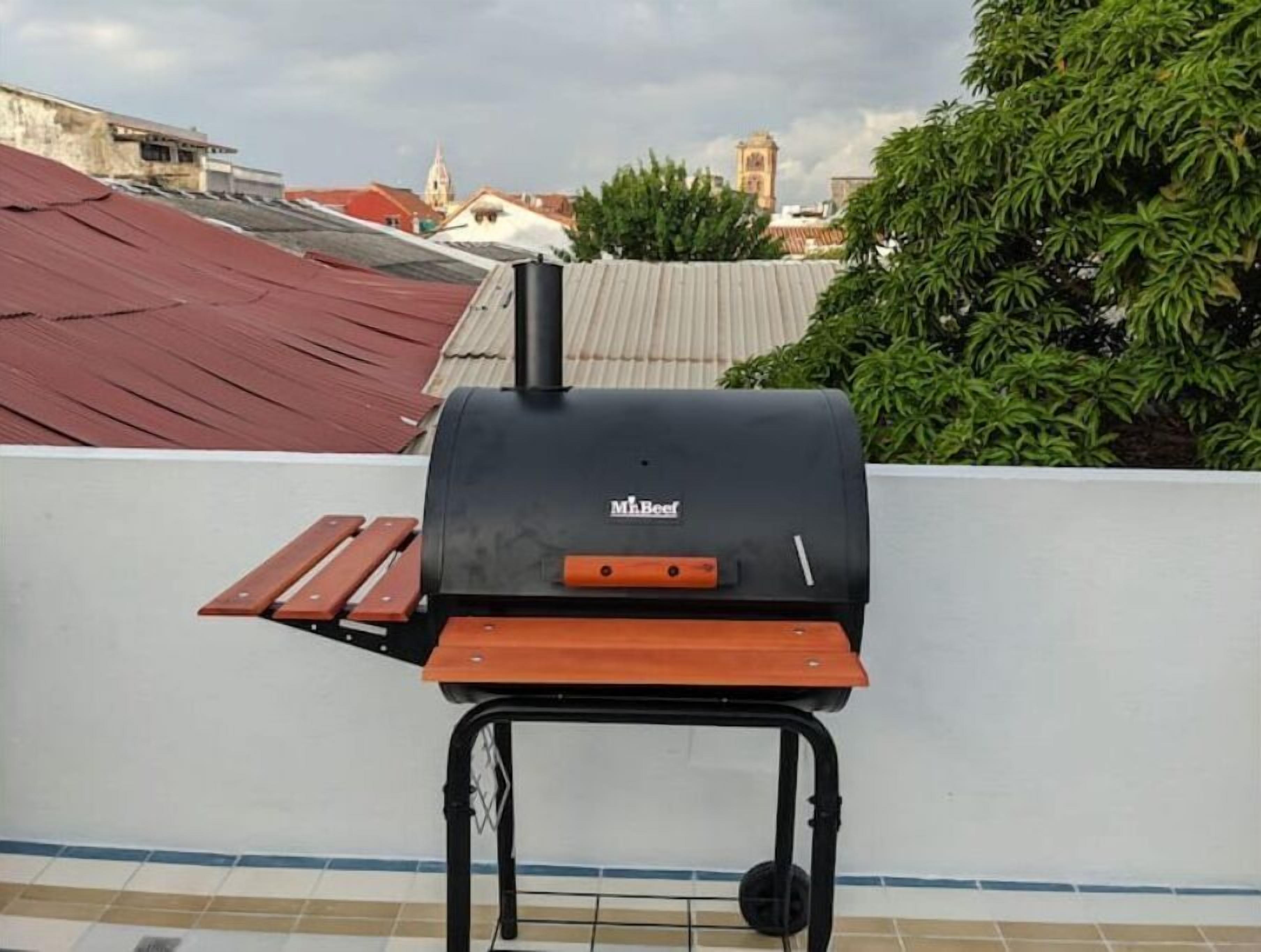 A portable barbecue grill on a rooftop with a view of buildings and a church steeple in the background.