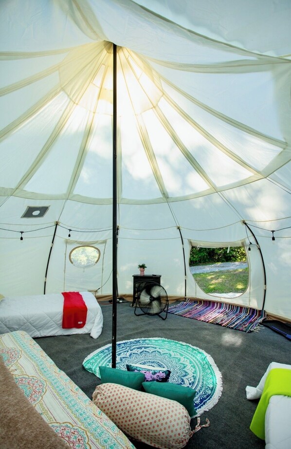 Una tenda con un letto, una ventola, una finestra e vista sulla natura.