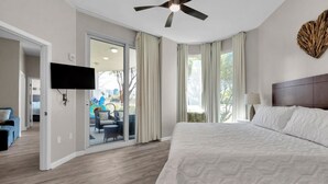 A hotel room with a large bed, a ceiling fan, a TV mounted on the wall, and a view of the outdoor area through a sliding glass door. - Rare end unit at the Palms of Destin w/ 2 King beds Steps from the Pool
 (Destin)
