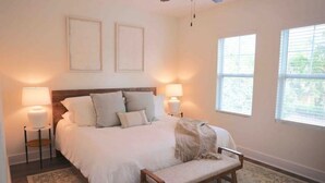A bedroom with a bed, bedside lamps, a bench, and two windows. - Cozy 2-Story House in Historic Downtown Wilmington. Walk to weddings & concerts! (Wilmington)