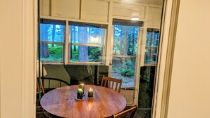 A round wooden table with two candles, surrounded by chairs, in a room with large windows offering a forest view. - Solitude in a cozy cabin on the Wisconsin River (Rhinelander)