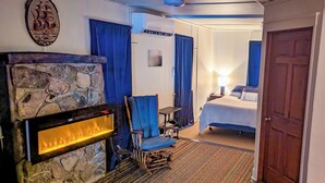 Ein Hotelzimmer mit Kamin aus Stein, einem Bett, einem Schreibtisch und einem Sessel.
