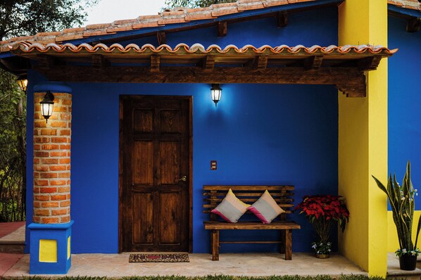 A building with a wooden door, a bench with cushions, and a potted plant. - Villas Na (San Cristóbal de las Casas)