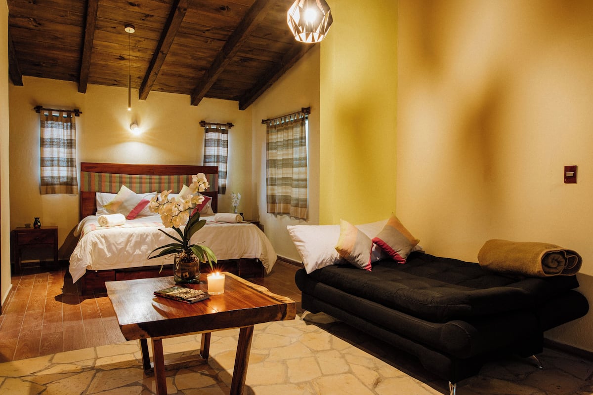 A bedroom with two beds, a wooden ceiling, a black sofa, and a small table with a candle.