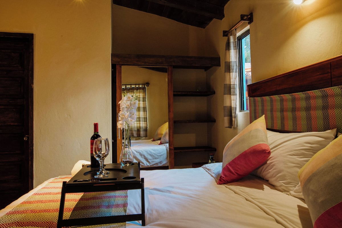 A hotel room with a bed, a bedside table with a wine glass and bottle, and a window with curtains.