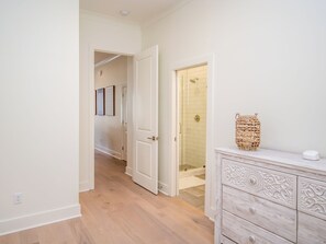 Un couloir avec un plancher en bois, une porte blanche et une salle de bain dotée d’une porte de douche en verre.