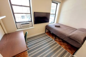 Une petite pièce comprenant un lit, un bureau, une chaise, un téléviseur et une fenêtre.