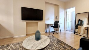 A modern living room with a flat-screen TV, a round marble table, a black office chair, and a large mirror.