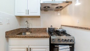 A kitchen with white cabinets, a granite countertop, a gas stove, and a stainless steel range hood.