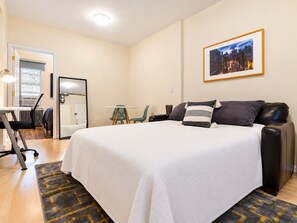 A hotel room with a large bed, a desk, a chair, and a view of the city at night.