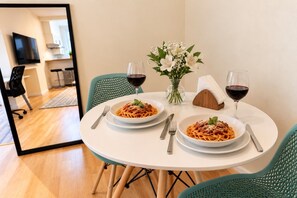 A dining table with two plates of spaghetti, two wine glasses, and a vase of flowers.