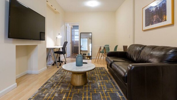 A living room with a leather sofa, a TV mounted on the wall, a round coffee table, and a patterned rug.