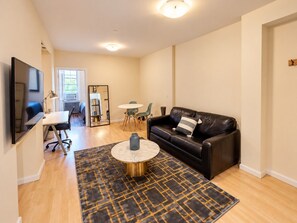 A modern living room with a black leather sofa, a round coffee table, and a TV mounted on the wall.