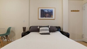 A bedroom with a bed, a chair, a coat rack, and a framed picture on the wall.