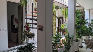 A corridor with hanging plants, a wooden staircase, and a white chair. - Walled City 2-bedroom 2-bath Condo with Patio (Cartagena de Indias)