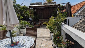 En tagterrasse med udendørs møbler, plantekasser og en grill.