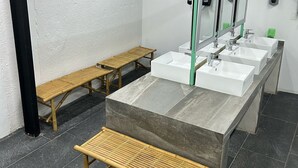 A modern restroom with three sinks, two benches, and a large mirror. - Green Caps Cancún Hospedaje (Cancun)