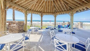 A wooden gazebo with tables and chairs, overlooking a beach. - Family favorite! On the beach! Amazing amenities! (Orange Beach)