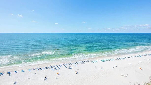 A beach with rows of umbrellas and beach chairs, a clear sky, and calm ocean waters. - Family favorite! On the beach! Amazing amenities! (Orange Beach)