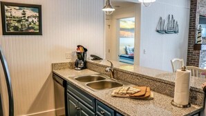 A kitchen with granite countertops, a double sink, and a view of a balcony with sailboats.