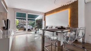 Un espace repas moderne avec une table et des chaises en verre, un mur d’accent en bois et une vue sur un jardin, visible à travers des portes vitrées.