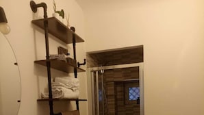 A bathroom with two sinks, a shower, and a toilet. There are shelves with towels and toiletries. - Cornflower House (San Benedetto del Tronto)