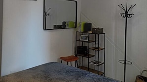 A room with a bed, a desk with a chair, a mirror, a coat rack, and a shelf with various items. - Cornflower House (San Benedetto del Tronto)