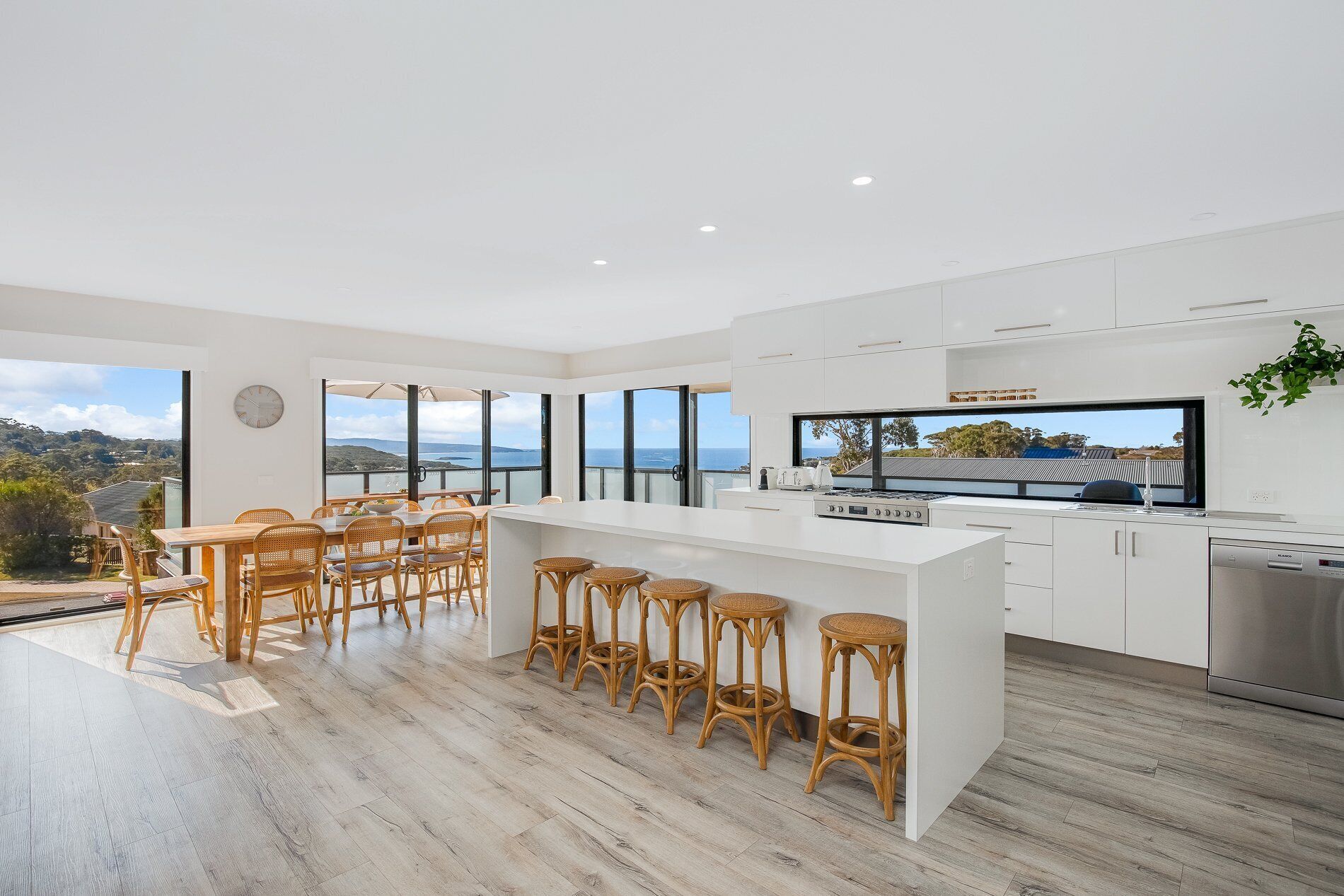 A modern kitchen with a large island, white cabinetry, and a view of the sea.