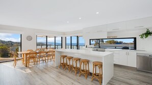 Une cuisine moderne dotée d’un grand îlot central, de meubles blancs et offrant une vue sur la mer.