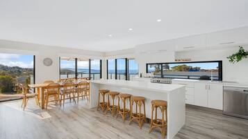 A modern kitchen with a large island, white cabinetry, and a view of the sea.
