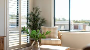 A clear view of a room with a wooden table, a glass vase with green foliage, a chair, and a window with blinds.