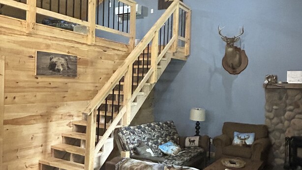 Un intérieur rustique avec un escalier en bois, une tête de cerf accrochée au mur, un canapé agrémenté de coussins à motifs animaliers et une cheminée en pierre.