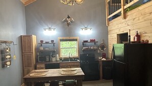 Une cuisine rustique avec des meubles en bois, une table à manger avec des chaises, un lustre et une vue sur l’extérieur par une fenêtre.