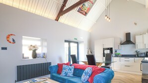 A modern interior with a blue sofa, wooden coffee table, and a kitchen area. - Mayfield Cottage (Malmesbury)