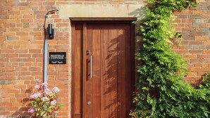 A brick building with a wooden door, a sign reading "Mayfield Cottage", and potted plants beside the entrance. - Mayfield Cottage (Malmesbury)