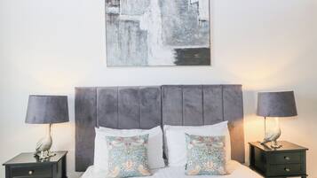 Una cama bien hecha con un cabecero gris, dos mesitas de noche con lámparas y almohadas decorativas.