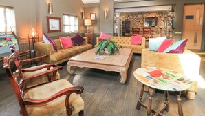 A spacious living room with a wooden ceiling, a fireplace, and a stone wall. There are multiple seating areas with plush sofas and armchairs. - Mayfield Cottage (Malmesbury)