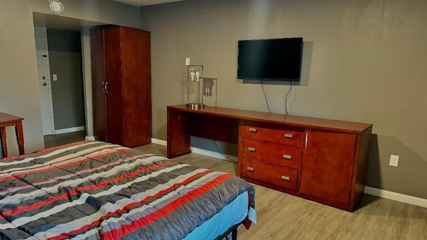 A bedroom with a bed, a wooden desk, a television, and a wardrobe. - Budget Inn New Cumberland-Harrisburg-Hershey-York (New Cumberland)