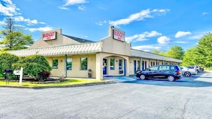 A Budget Inn with a single-story structure, a parking lot, and a row of parked cars. - Budget Inn New Cumberland-Harrisburg-Hershey-York (New Cumberland)