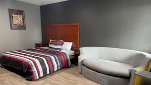 A hotel room with a bed, a chair, a nightstand, and a framed picture on the wall. - Budget Inn New Cumberland-Harrisburg-Hershey-York (New Cumberland)