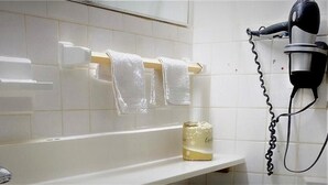 A bathroom with a bathtub, a towel rack with two white towels, a bottle of lotion, and a hairdryer on a wall-mounted stand. - Budget Inn New Cumberland-Harrisburg-Hershey-York (New Cumberland)