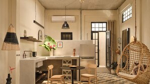 A compact kitchen with a checkered floor, a dining table with chairs, a hanging light fixture, and a wicker chair. - PAZ by DW (San Juan)