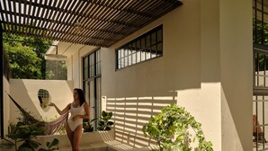 A woman in a white swimsuit standing on a concrete staircase with plants around. - PAZ by DW (San Juan)