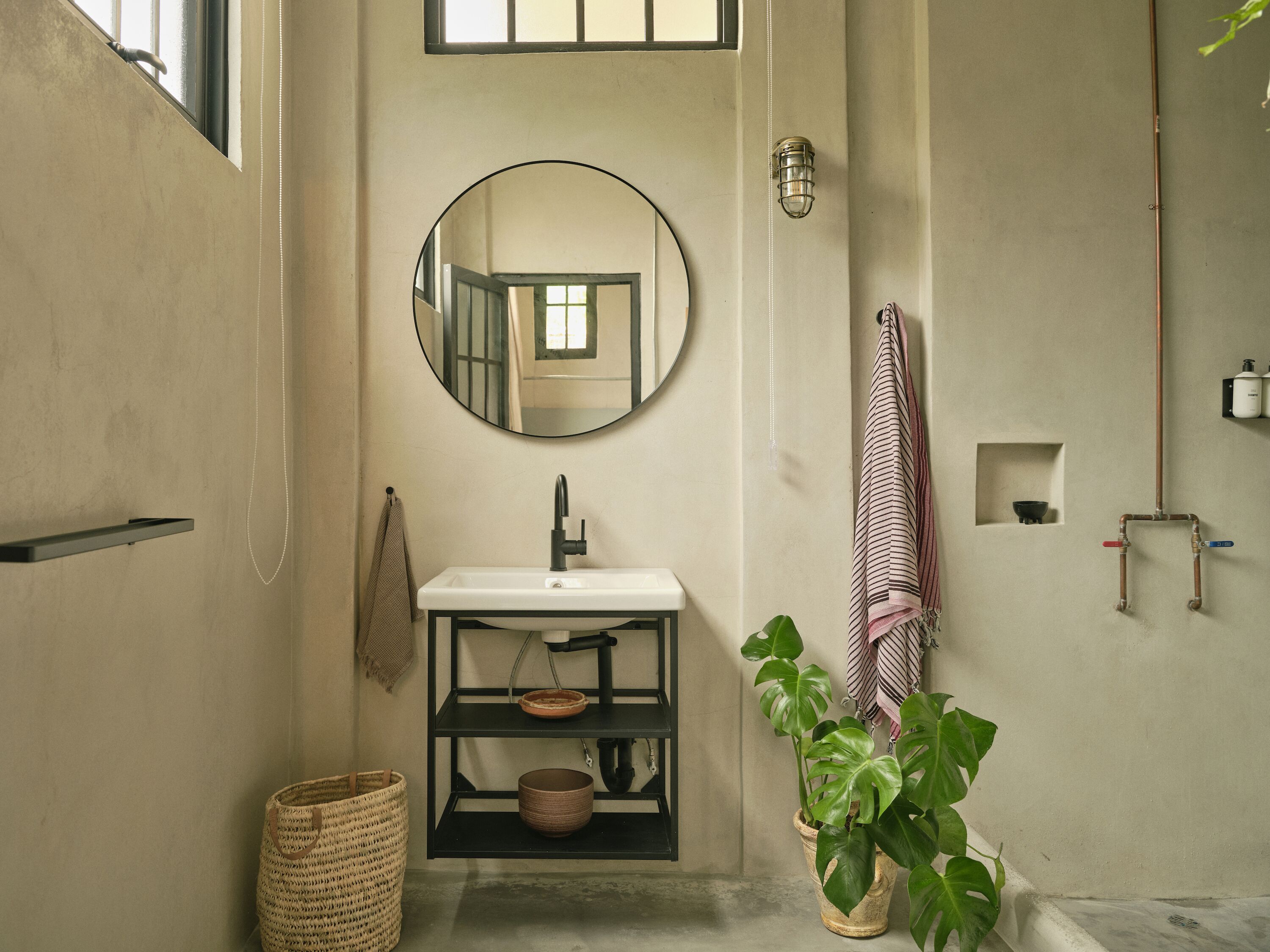 A bathroom with a round mirror, a sink, a shelf with a bowl, a potted plant, and a towel hanging on a rack.