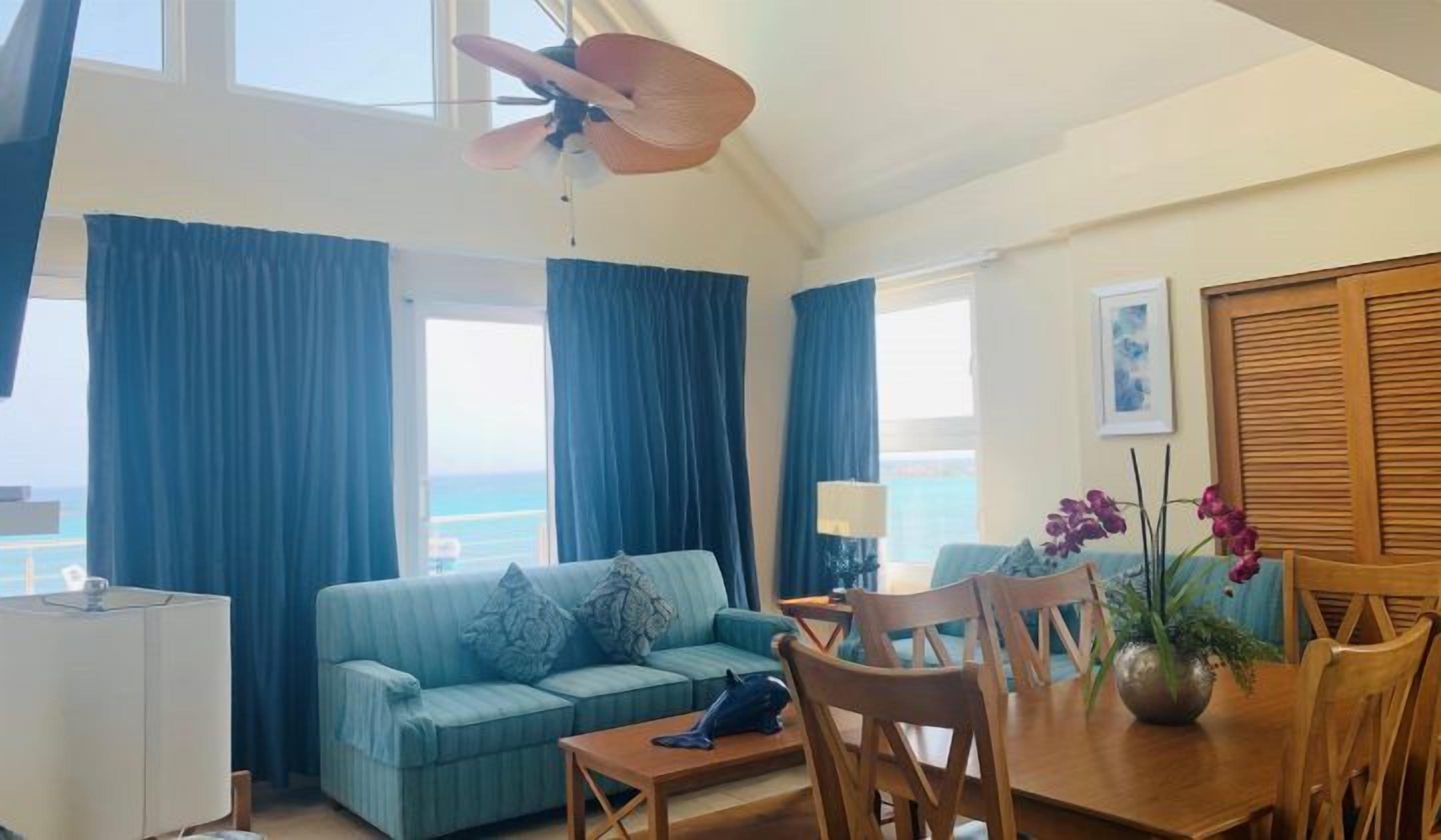 A room with a sofa, dining table, chairs, and a ceiling fan.