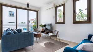 A modern living room with a sofa, chairs, a TV, and large windows.