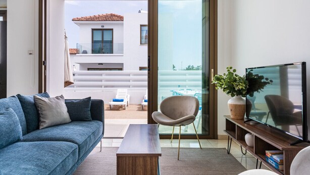 A modern living room with a sofa, a coffee table, a TV, and a sliding glass door leading to an outdoor seating area.